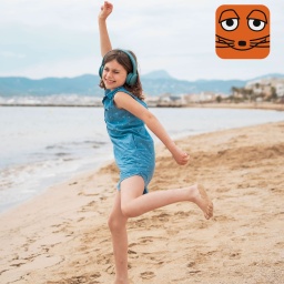 Ein Mädchen tanzt am Strand und hört mit Kopfhörern Musik.