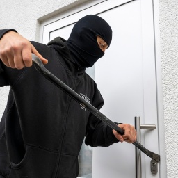 Eine maskierte Person versucht eine Haustür aufzubrechen (Symbolbild).