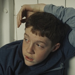 Szene aus dem Film "Mit der Faust in die Welt schlagen": Ein Junge sitzt zwischen zwei Pissoirs