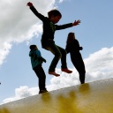 Kinder springen auf einer Hüpfburg und heben sich dabei als Schatten vom Himmel ab.