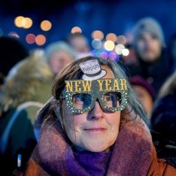 Eine Frau in einer Menschenmenge trägt eine bunte Pappbrille mit der Aufschrift "Happy New Year".