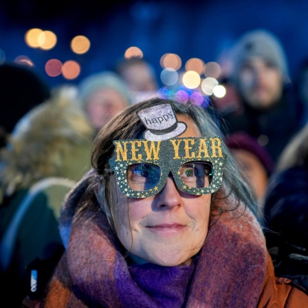 Eine Frau in einer Menschenmenge trägt eine bunte Pappbrille mit der Aufschrift "Happy New Year".