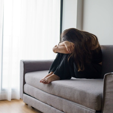 Junge Frau sitzt zusammengesunken auf dem Sofa, ihr Gesicht ist nicht zu erkennen