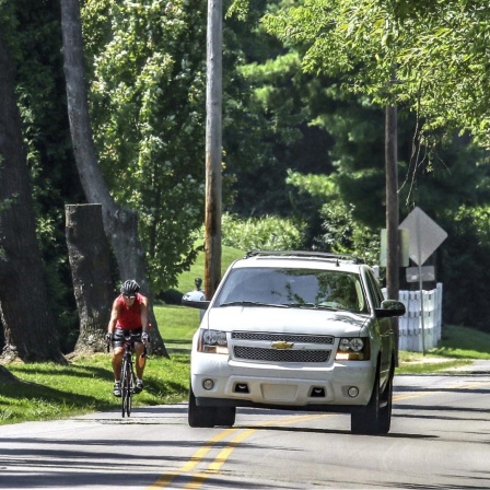 Fahrradfahrer und SUV im Grünen auf der Straße nebeneinander.