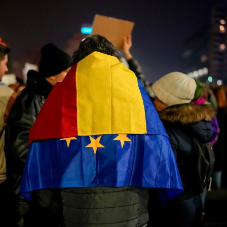 Ein Mann mit der rumänischen und der EU-Fahne über den Schultern nimmt an einem Protest gegen Georgescu, den unabhängigen Kandidaten für das rumänische Präsidentenamt, der die erste Wahlrunde gewonnen hat.