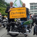 Jörgen S. Rasmussen und Carl Hahn stehen an einer DKW SB 200 von 1936 vor dem einstigen Motorradwerk von DKW und MZ in Zschopau mit dem neuen Ortseingangsschild der Motorradstadt.