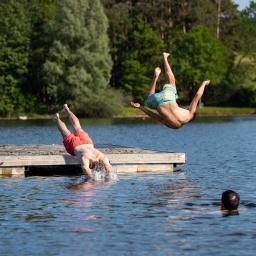 Jugendliche springen von einer Schwimminsel in einen See (Bild: picture alliance/dpa/Daniel Karmann)