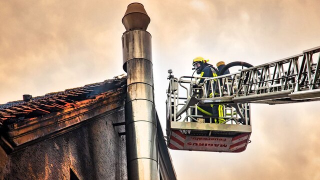 Zwei Feuerwehrmänner auf einer Drehleiter löschen einen Brand unter einem Dach