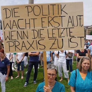 Eine Ärztin hält bei einer Demonstration ein Schild hoch mit der Aufschrift "Die Politik wacht erst auf, wenn die letzte Praxis zu ist".