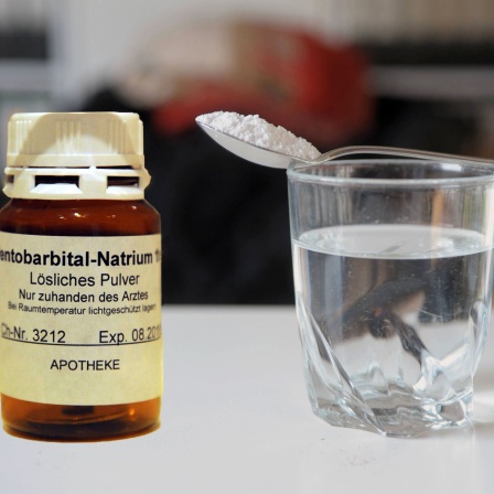 kleines Gefäß mit der Aufschrift Pentobarbital-Natrium, daneben ein Glas mit Wasser, darauf ein Löffel mit weißem Pulver.