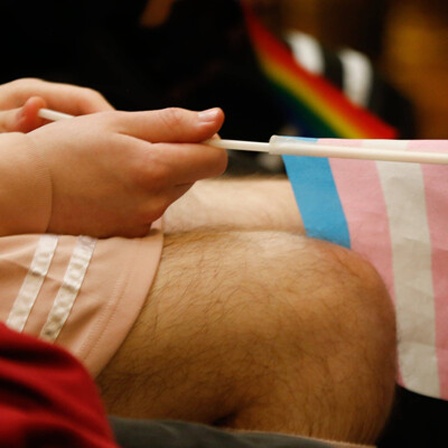 Eine sitzende Person hält eine Transgender-Flagge in der Hand