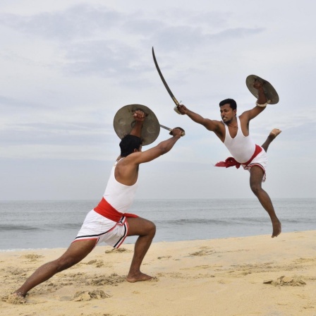 Zwei Kalaripayattu Kämpfer mit langen Säbeln und runden Schildern in Aktion
