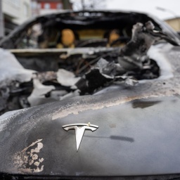 Verkohlte Frontpartie eines ausgebranntes Autos, auf der Motorhaube erkennt man noch das Logo der Marke Tesla. 