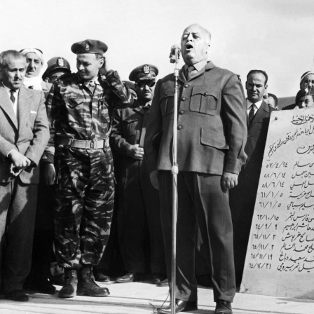 Historisches Schwarzweißfoto von Ahmed Shukeiri, der auf einer Bühne in ein Mikrofon spricht.