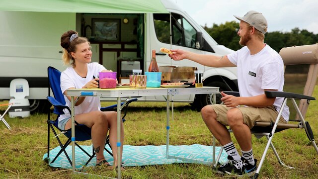 Von Campingbus bis Luxusvan: Zwei Personen sitzen vor einem Campingvan an einem gedeckten Campingtisch.
