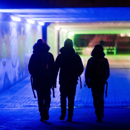 Drei Jungen gehen am frühen Morgen durch eine bunt-beleuchtete Unterführung zur Schule