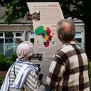 Eine Frau und ein Mann stehen vor der Gedenktafel zur Kongokonferenz in der Berliner Wilhelmstraße. 