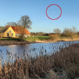 Am frühen Morgen steht der Mond über einem Haus an einem Fluss.