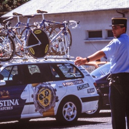 Tour de France 1998: Ein Fahrzeug des Teams Festina mit Rädern auf dem Dach wird von einem Polizisten eingewiesen. 