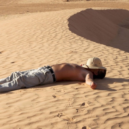 Das Zittern des Fälschers - Ein Mann liegt im Sand in Sahara