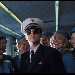 Ein Filmstill aus &#034;Catch Me If You Can&#034; (2002): Der Hochstapler Frank (Leonardo DiCaprio) in einer Piloten-Uniform von PanAm, umringt von lächelnden Stewardessen