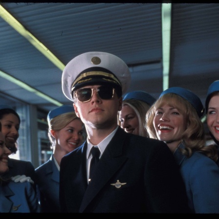 Ein Filmstill aus &#034;Catch Me If You Can&#034; (2002): Der Hochstapler Frank (Leonardo DiCaprio) in einer Piloten-Uniform von PanAm, umringt von lächelnden Stewardessen