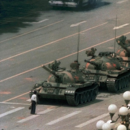 Ein chinesischer Mann steht auf einer breiten Straße vor einer Panzerkolonne, um sie aufzuhalten.