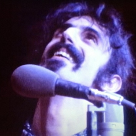 Frank Zappa bei einem Konzert blickt lächelnd nach oben.