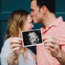 Ein Paar hält gemeinsam ein Ultraschallbild eines Neugeborenen in die Kamera.
