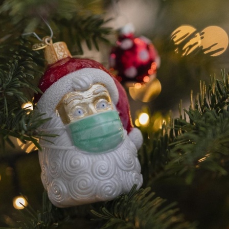 An einem Weihnachtsbaum hängt Weihnachtsschmuck in Form eines Weihnachtsmannes, der eine Maske trägt. 