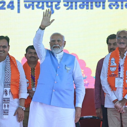 Der indische Premierministers Narendra Modi steht auf einer Bühne. Er hat eine Hand zum Gruß erhoben. 