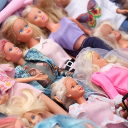 Mehrere klassische Barbie-Puppen in verschiedenen Puppenkleidern liegen auf einer Fläche.