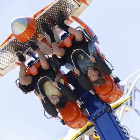 Teenager fahren mit dem Kopf nach unten auf einem Karussell. (Bild: IMAGO/imageBROKER/Svetlana)