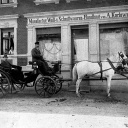 Eine Kutsche steht vor einem Geschäft. In der Kutsche sitzt August Karlowsky.