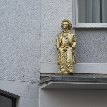 Goldene Beethovenfigur auf einem Sims an einer Wohnhausfassade.