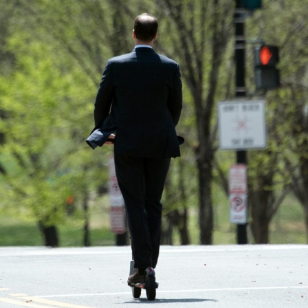 Ein Mann fährt im Anzug auf seinem Elektroroller über eine Hauptstrasse in Washington DC.