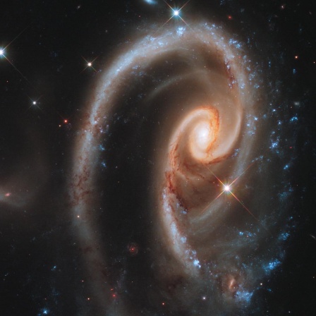 Ein Wirbel im Weltraum, im Inneren rötlich, außen Blautöne. Nach links eine Art Schweif. Zusammen ergibt es eine liegende Rose.