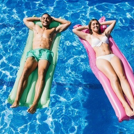 Zwei junge Menschen auf Luftmatrazen im Pool.