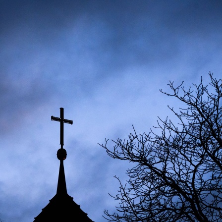 Dunkle Wolken ziehen über das Kreuz auf einer evangelischen Kirche hinweg; © picture alliance/dpa/Julian Stratenschulte