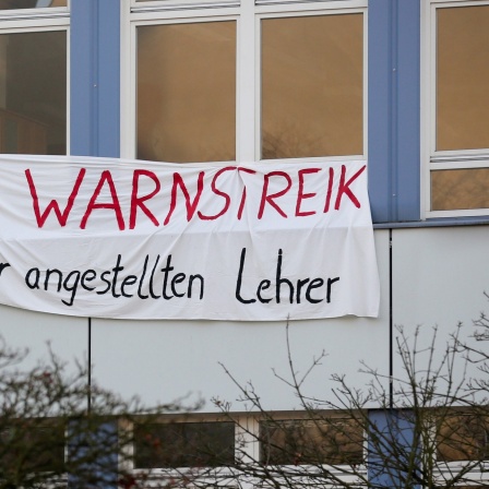 Ein Transparent mit der Aufschrift "Warnstreik der angestellten Lehrer" hängt am Gebäude einer Schule.