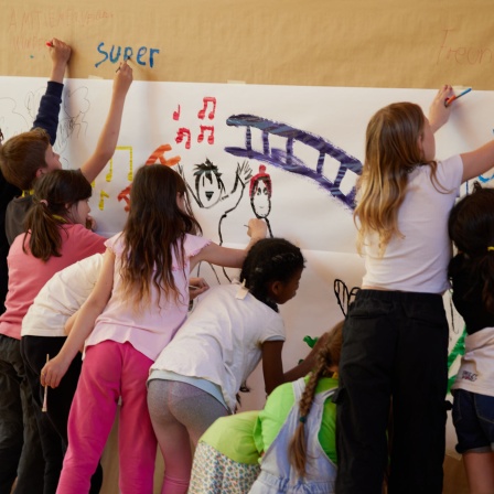 Schülerinnern und Schüler bemalen eine Leinwand. (Quelle: Picture Alliance)