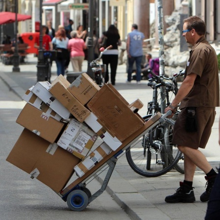 Paketzusteller liefert Pakete auf einem vollbeladenen Karren aus.