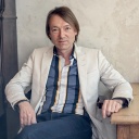Musiker Jochen Distelmeyer sitzt an einem Holztisch vor einer Wand.