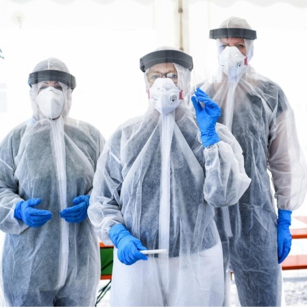 Drei Mitarbeiter vom Gesundheitsamt in Berlin Mitte stehen in Schutzkleidung, in der ambulanten Corona-Test- Einrichtung. 