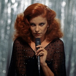 Die Sängerin Milva, wegen ihrer roten Haare auch &#034;La Rossa&#034; genannt, tritt mit Mikrofon in der Hand vor einem glitzenden Hintergrund auf.