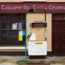 Das Schild einer Tankstelle und eines Pubs sind in gälischer Sprache verfasst. Im Vordergrund ist eine Zapfsäule.