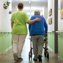 Eine Pflegefachkraft geht mit einer Bewohnerin durch das Seniorenheim