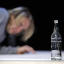Schauspieler Mirco Kreibich liegend auf der Bühne des DT in Berlin. Er schaut auf eine Flasche Hochprozentiges.