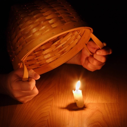 Hände halten Korb über Kerze: Warum sagt man: &#034;Stell dein Licht nicht unter den Scheffel&#034;?