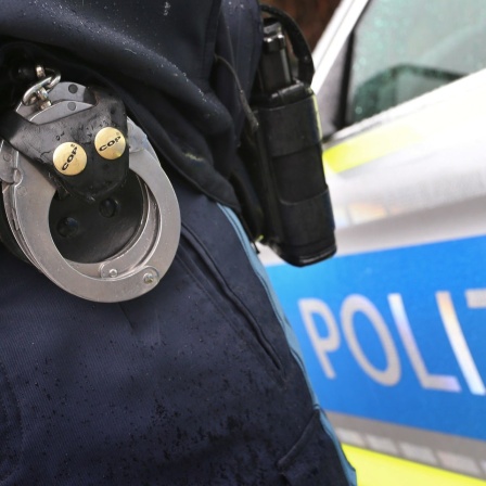 Ein Polizist trägt Handschellen und eine Waffe.